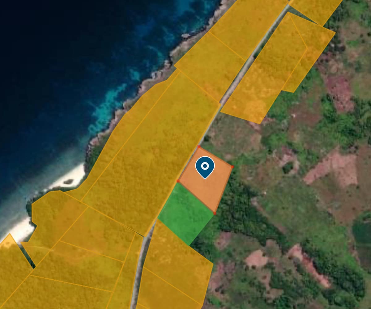 A high-resolution aerial view of two separate, rectangular land parcels situated next to each other within a dense green forest. A paved asphalt road borders the plots, leading toward the turquoise waters of Halete Beach.