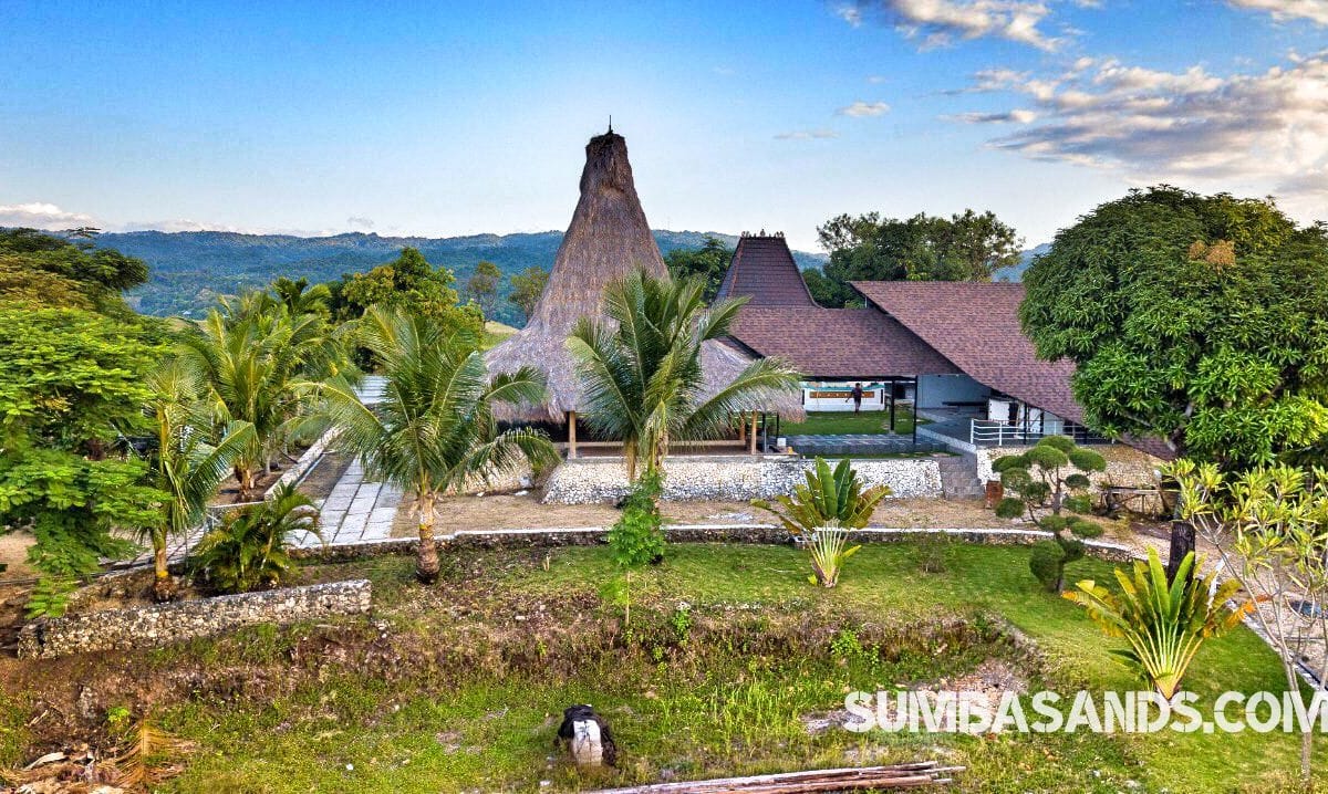 An aerial shot of the Tambolaka Hill Top Villa or Resort. The image captures the private road winding up to a 2-hectare peak, showcasing the 270sqm covered lounge surrounded by the deep green canopy of West Sumba’s lush forest