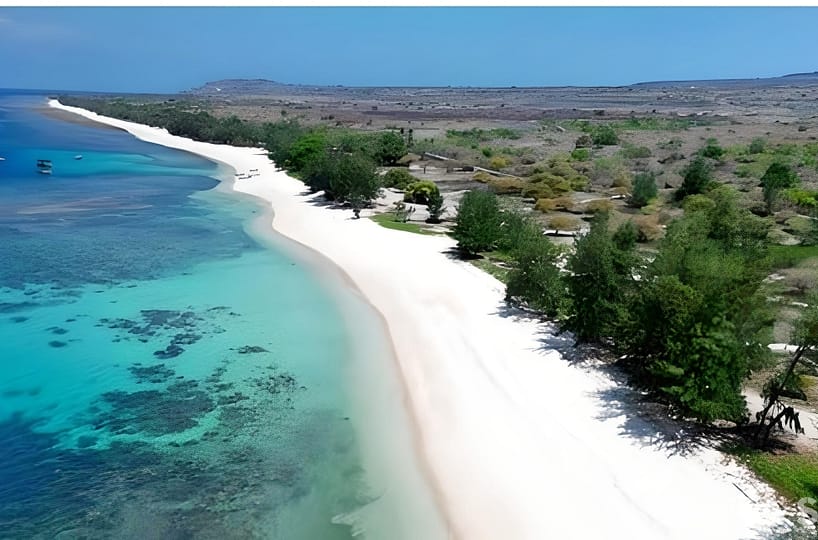 A wide aerial shot of the 2-hectare Puru Kambera Beachfront Legacy. The image captures the flat, pristine land meeting the crystal-clear turquoise waters, with the golden savanna hills and wild horses of Puru Kambera in the background.