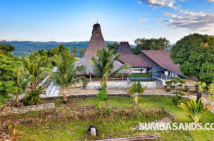 An aerial shot of the Tambolaka Hill Top Villa or Resort. The image captures the private road winding up to a 2-hectare peak, showcasing the 270sqm covered lounge surrounded by the deep green canopy of West Sumba’s lush forest