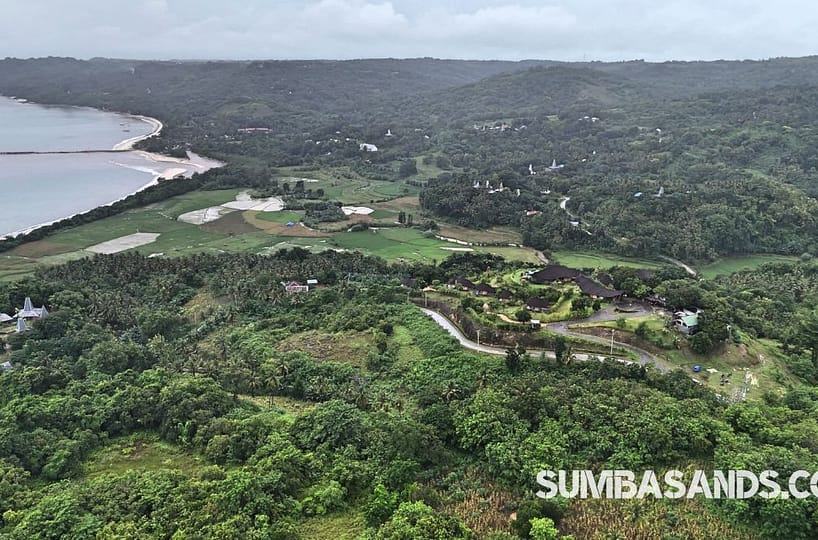 An aerial shot of the Ketanu Resort Neighbor Plot in Pahola. The image captures lush green hill and valley terrain overlooking the turquoise Indian Ocean in West Sumba.