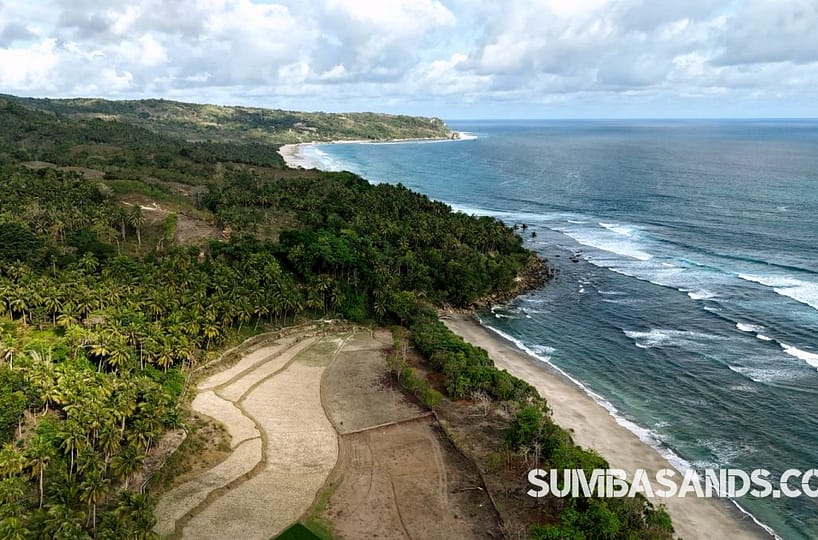 A dramatic aerial panorama of the Palamoko Nihiwatu Neighbor Plot. The image showcases the elevated hill plot with a direct line of sight to the iconic Nihiwatu shoreline and Palamoko Beach.