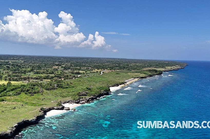 An aerial shot of the 6.5-hectare Kodi Private Beach Cliff Plot. The image captures a flat, rocky cliff overlooking a vibrant blue sea with three distinct private beach coves in West Sumba.