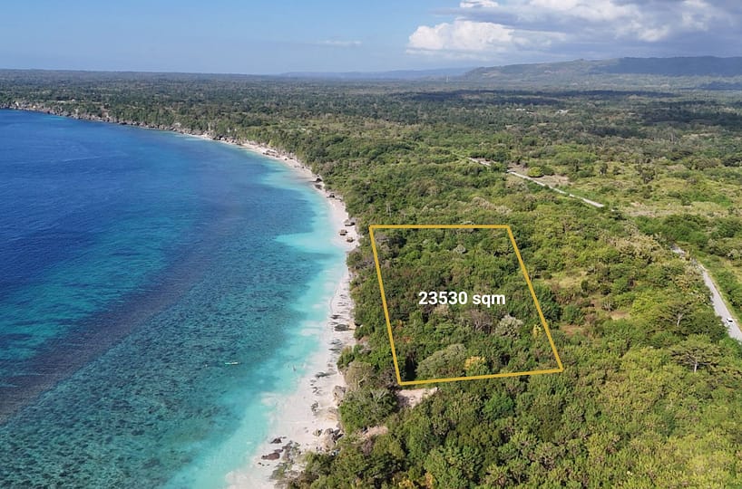 A spectacular high-angle aerial view showcasing the property's dramatic, elevated rocky crest dropping directly down onto a pristine, untouched white sand beach meeting clear turquoise coral waters.